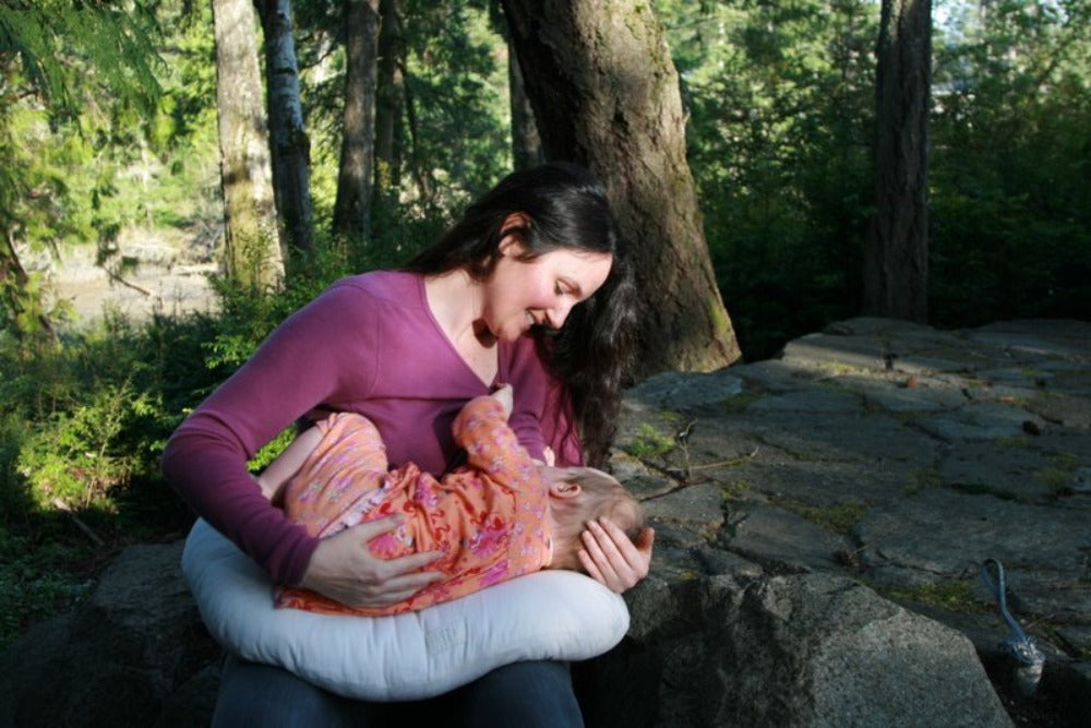 happy content mother nursing a baby laying on an all natural sustainably sourced eco wool stuffed nursing pillow that is encased in organic cotton