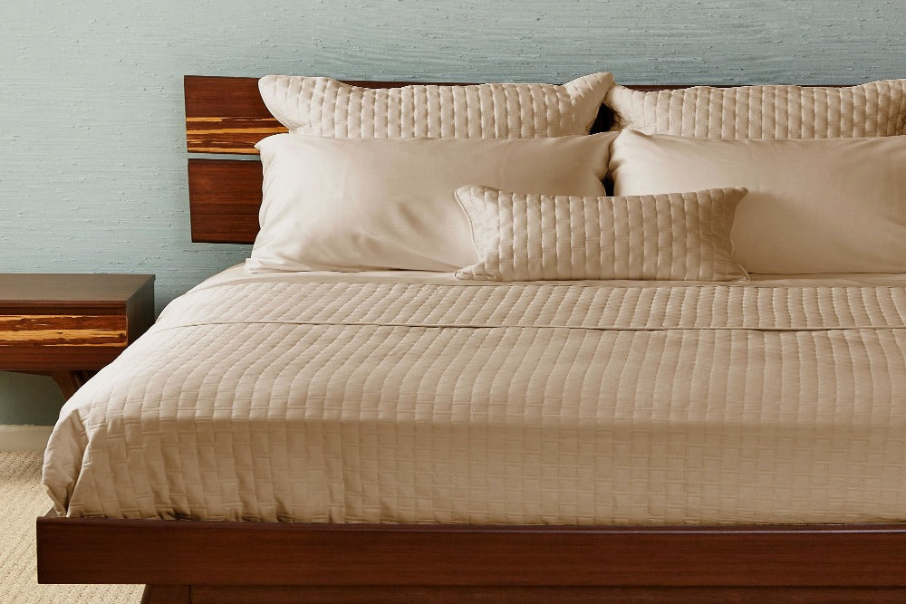A modern wood frame bed smartly made up with a Champagne Colored Luxurious 100% Bamboo Quilted Coverlet neatly tucked in and five matching pillows at the headboard