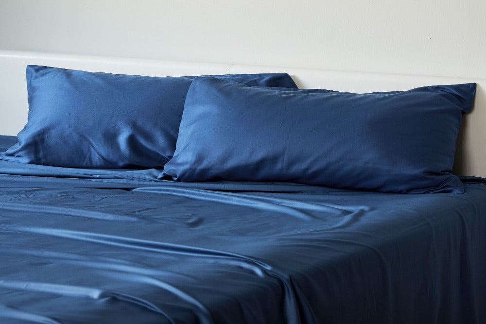 semi close up view of a bed made up with indigo colored silky smooth bamboo bedsheets and two matching pillows at the headboard