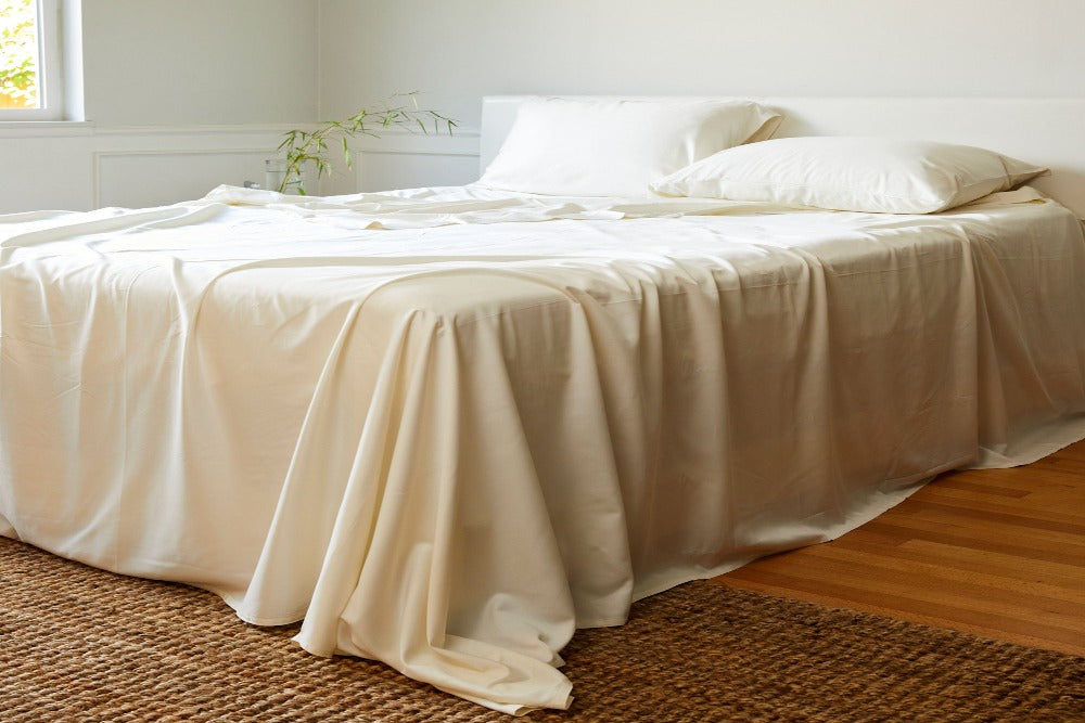 White bamboo bedsheets on an unmade queen size bed in a bright well decorated bedroom