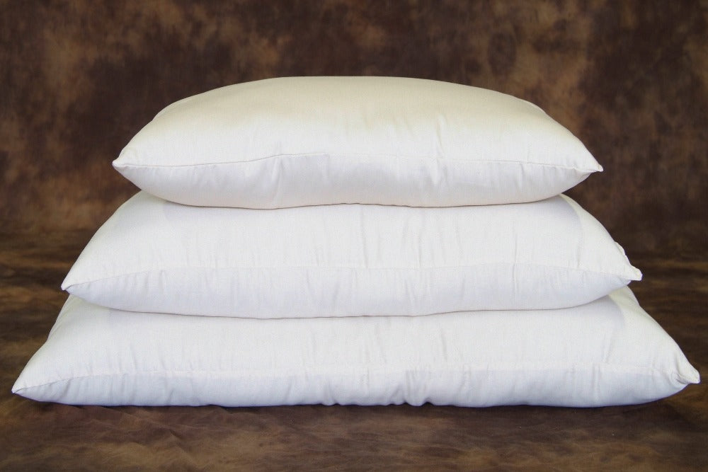 three natural colored natural organic pillows stacked by size and displayed on a brown bear skin rug