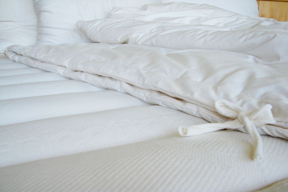 a folded natural colored all season organic comforter displayed on an unmade made
