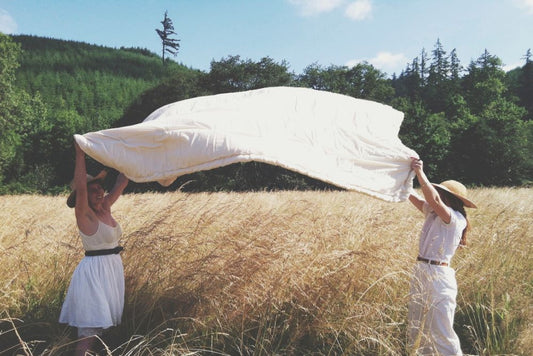 two happy girls in a mountain meadow lifting a certified organic cotton comforter filled with premium eco wool up into the breeze