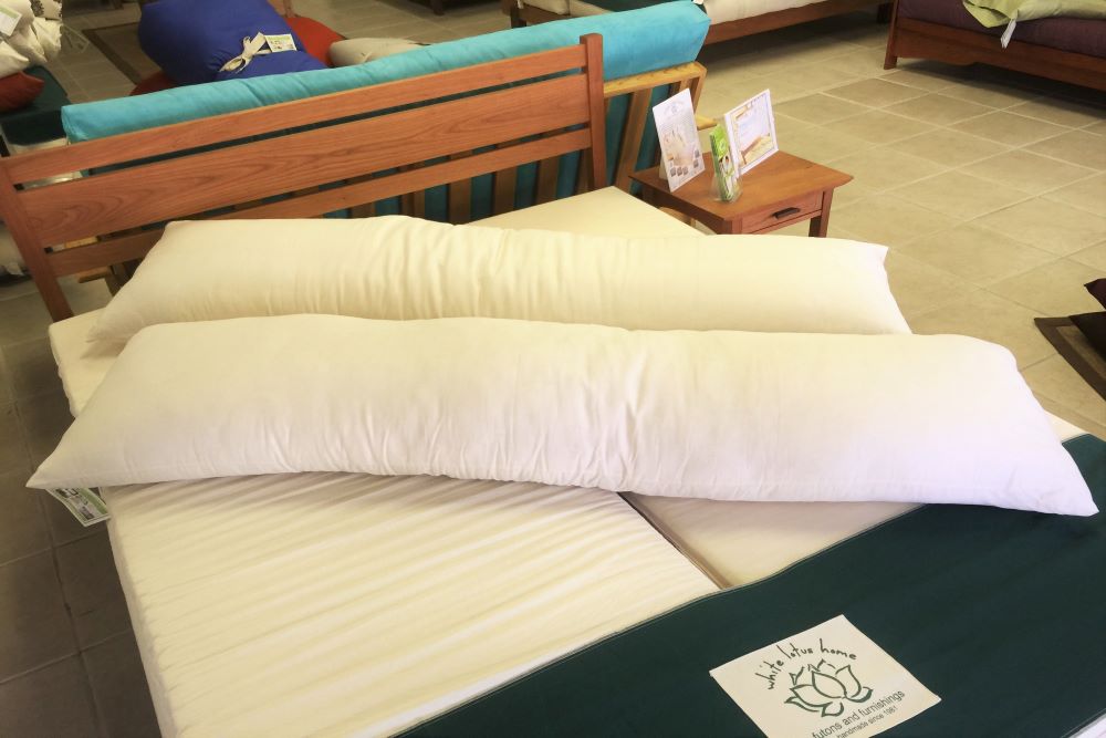 two body size natural latex stuffed pillows laying diagonally on a clean unmade bed