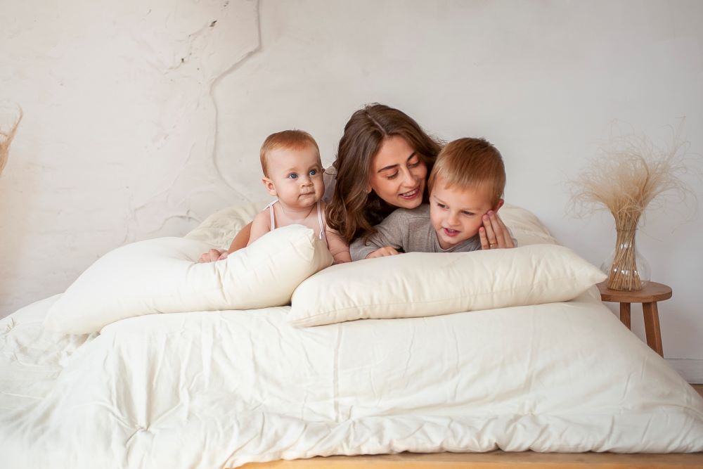 playful mother and two children playing on bed with their two eco wool filled sleep pillows 