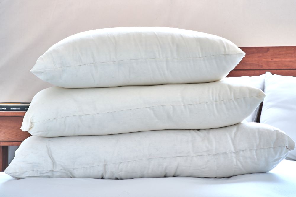 king size queen size and standard size sleep pillows stacked on clean unmade bed