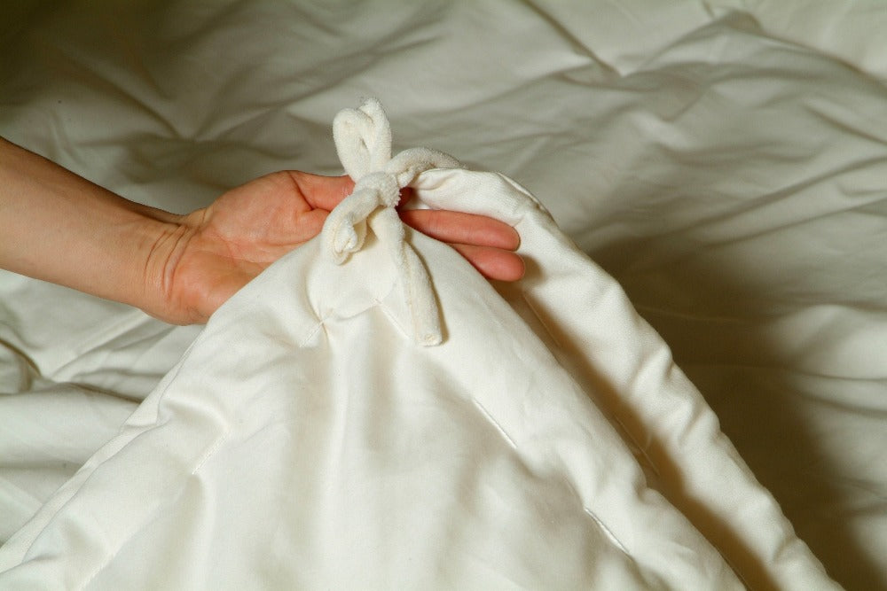 a hand holding the corner of an all season eco wool comforter displaying the corner ties of the comforter