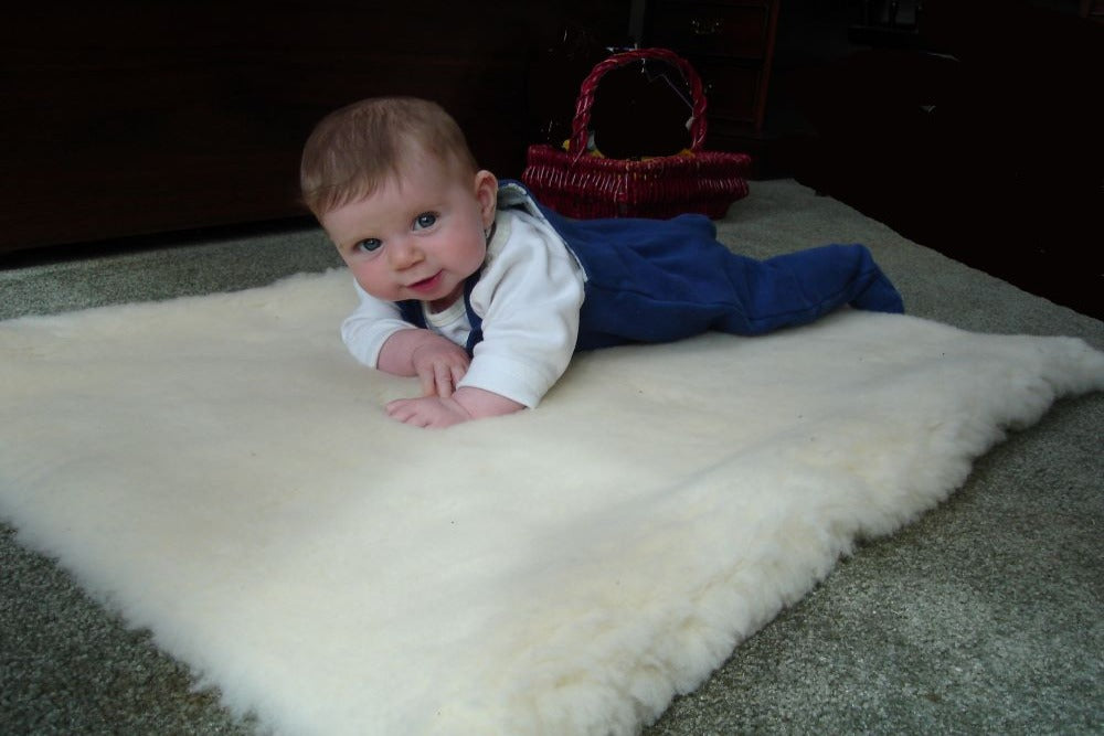 cute baby laying on bassinet size happy lamb fleece mattress topper displayed on a bed