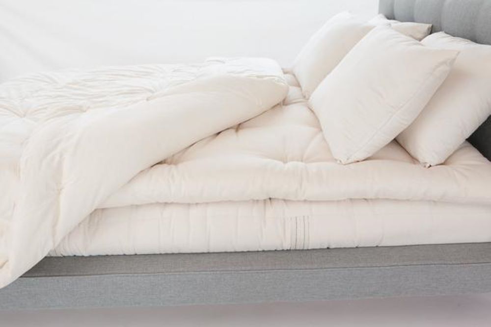 four all natural latex stuffed sleep pillows propped against the headboard of a bed covered with an organic mattress topper and natural cotton comforter that has the corner turned back