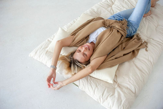 happy attractive woman laying on a quilted organic cotton comforter with a king size organic cotton sleep pillow under her head and her arms stretched out above her head