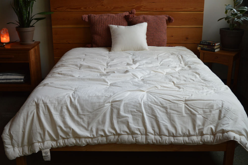 a natural colored GOTS certified organic cotton sateen comforter filled with premium eco wool spread over a modern wood framed bed in a well decorated bedroom