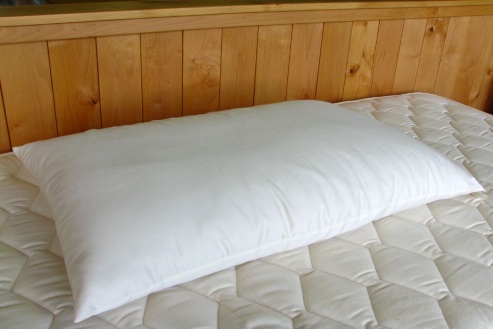 a king size premium eco wool filled pillow encased in organic cotton displayed on a clean unmade bed