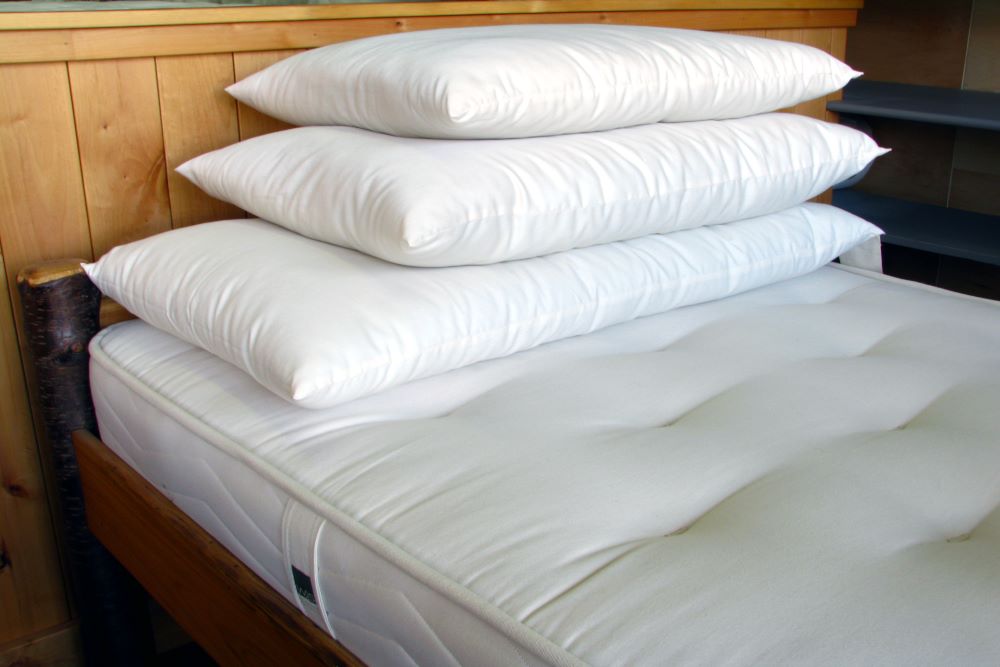 three stacked premium eco wool stuffed pillows encased in natural organic cotton sateen and displayed on a clean unmade bed