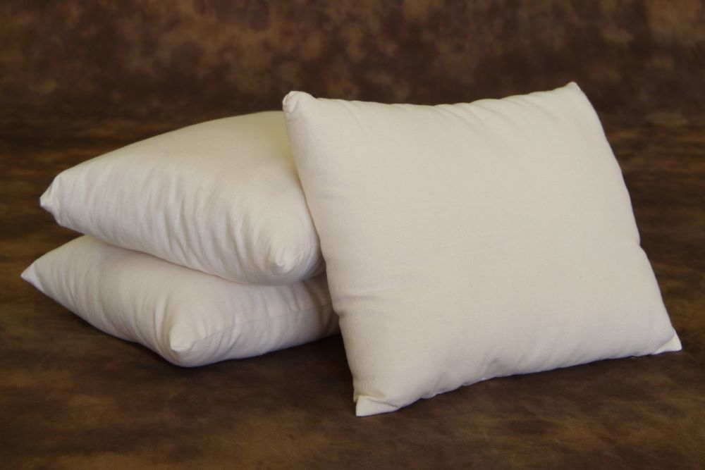 lose stack of three premium eco wool filled pillows encased in organic cotton pillow cases displayed on brown wool rug