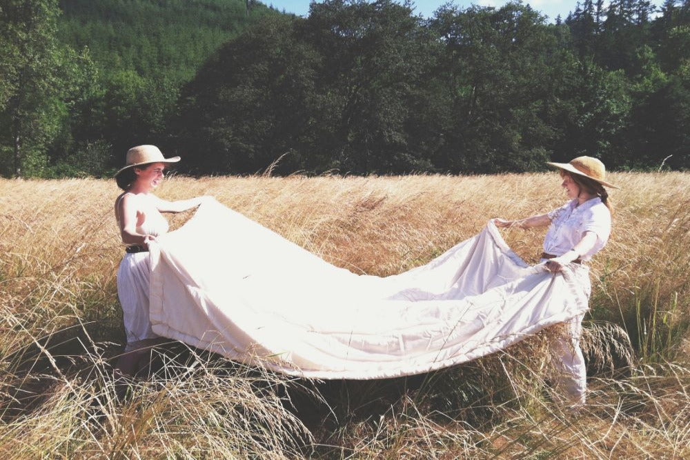 two women folding a natural colored certified organic comforter outside in a beautiful mountain meadow